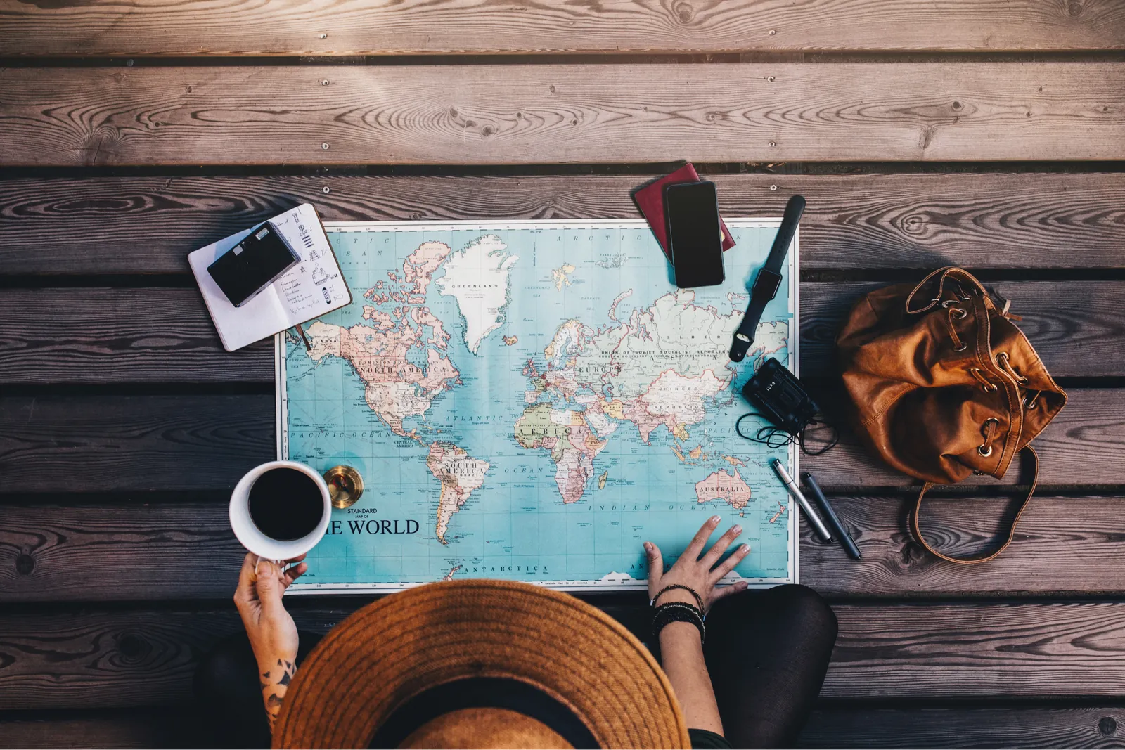Overhead view of a person planning with a world map, coffee and a hat