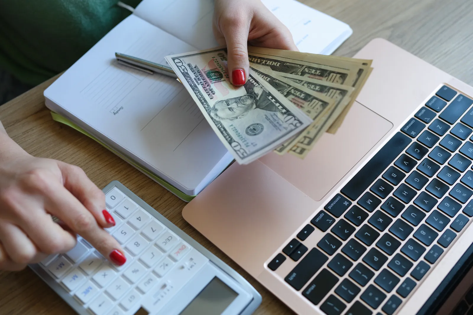 Hands counting cash beside a laptop and calculator