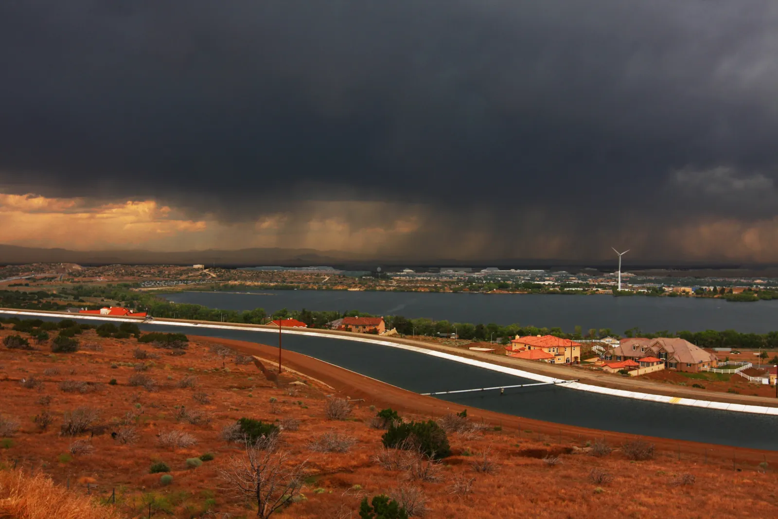 Dark storm clouds over the Antelope Valley high desert near Palmdale, with the California Aqueduct curving past homes and Lake Palmdale