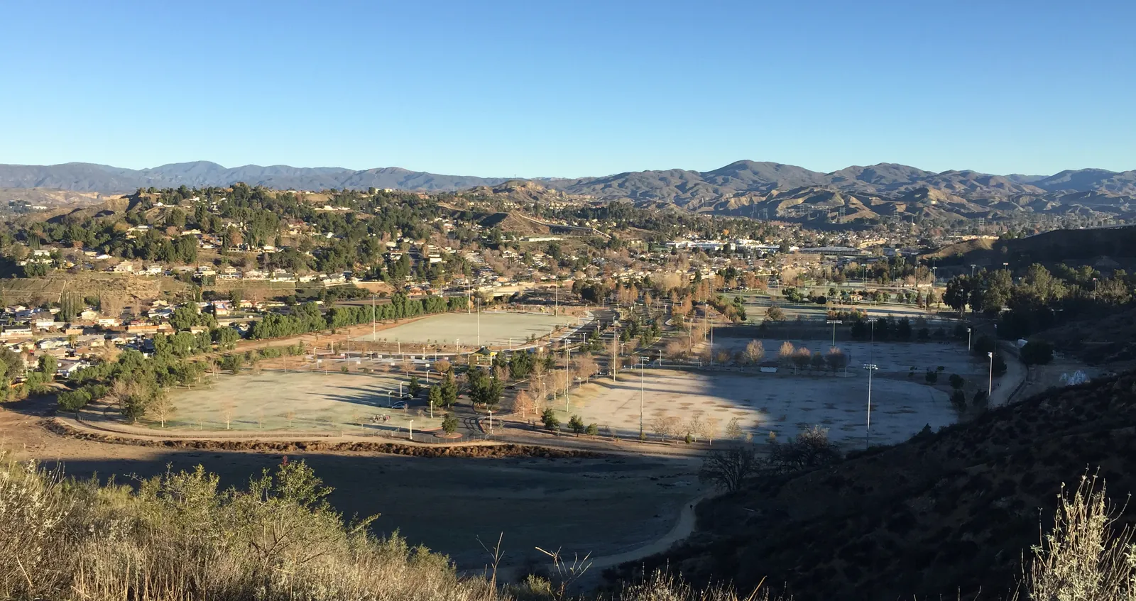 Frost-covered sports fields at Central Park in Saugus, Santa Clarita, seen from a hillside with homes and mountains beyond