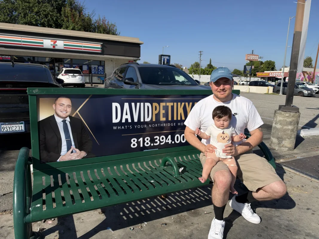 David Petikyan holding his baby on a bus bench showing his Northridge real estate ad at Balboa Blvd and Nordhoff St in Northridge