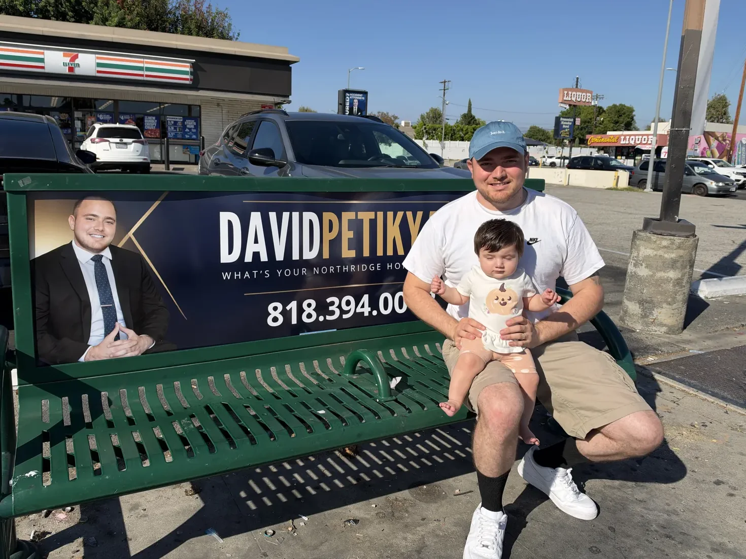 David Petikyan holding his baby on a bus bench showing his Northridge real estate ad at Balboa Blvd and Nordhoff St in Northridge