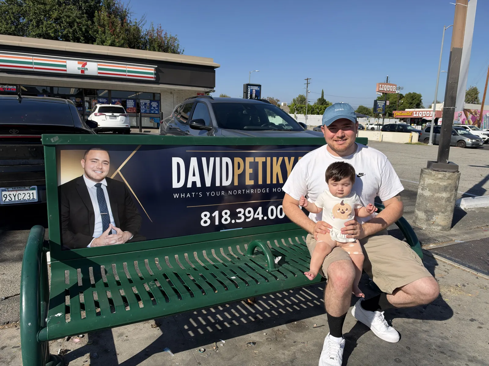 David Petikyan holding his baby on a bus bench showing his Northridge real estate ad at Balboa Blvd and Nordhoff St in Northridge