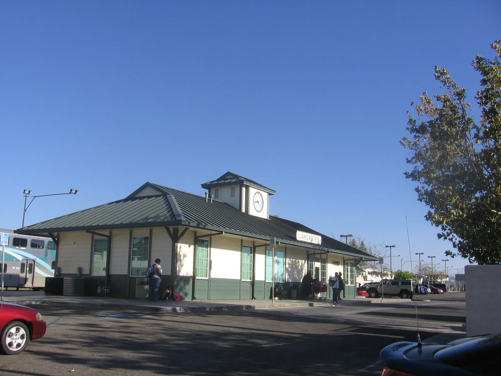 The green and white Lancaster Metrolink station building on Sierra Highway under a clear blue sky