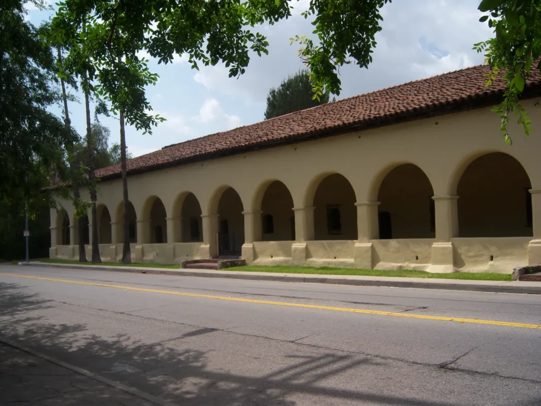 Arched colonnade of the convento building at Mission San Fernando Rey de España in Mission Hills, with palm trees along the street