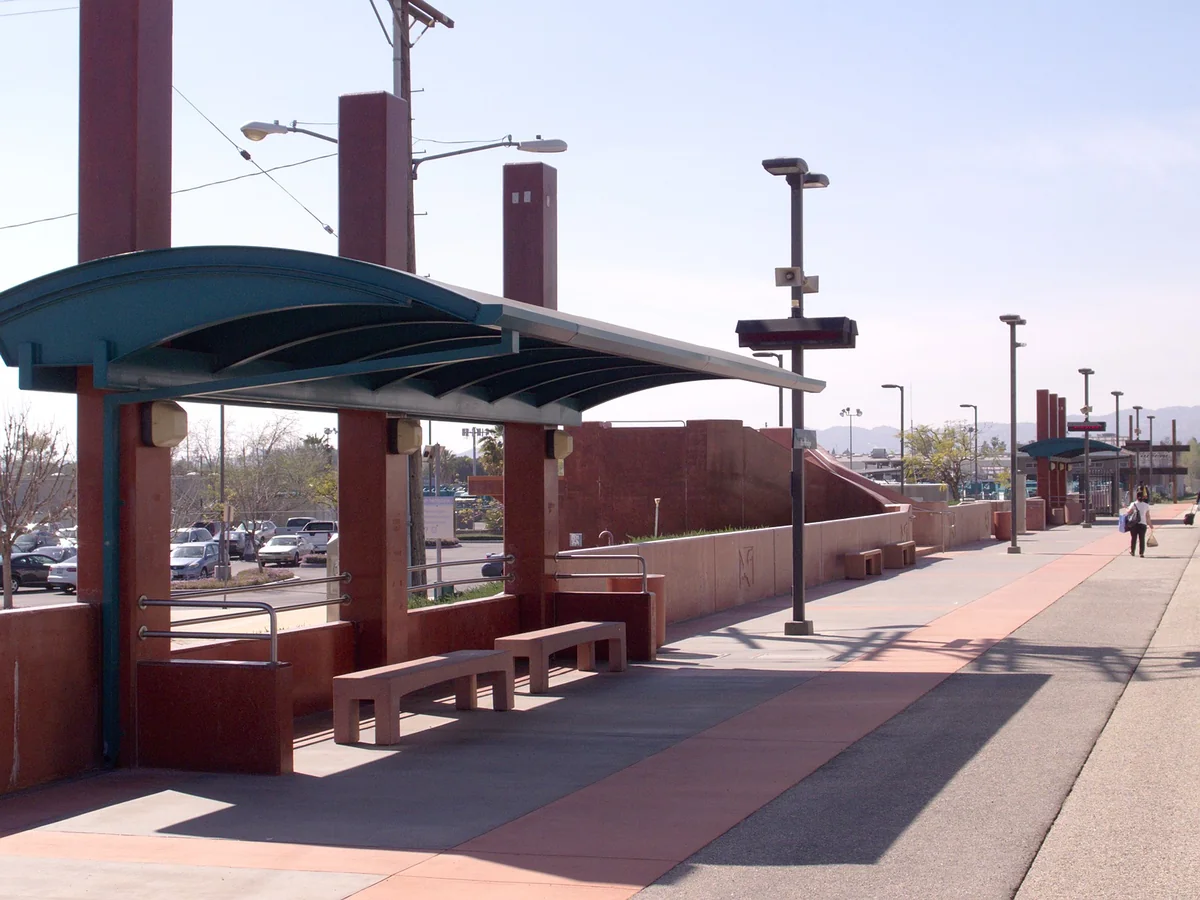 The Northridge Metrolink station platform with a curved teal canopy, red columns and benches, looking west along the tracks