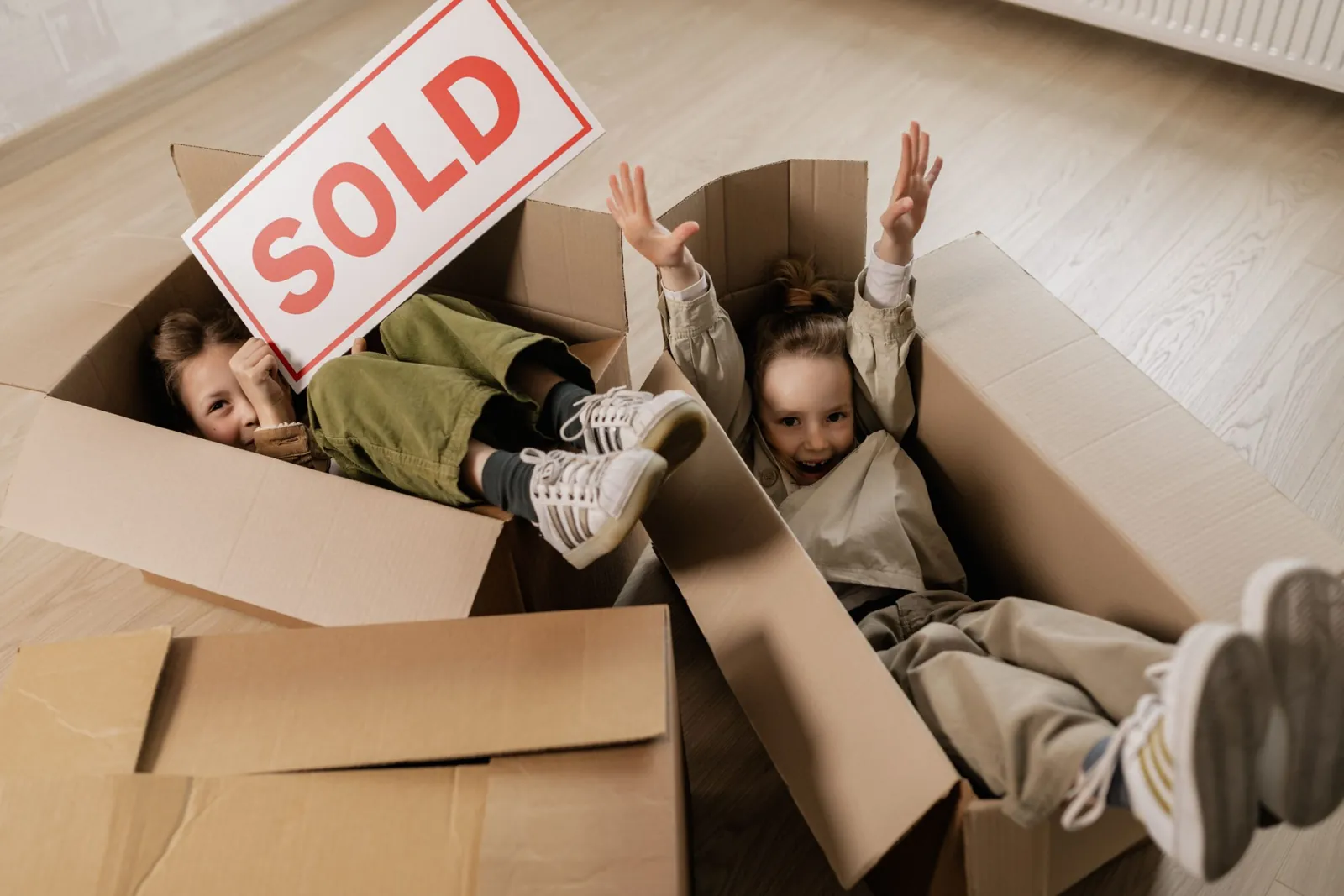 Kids playing in moving boxes under a 'Sold' sign