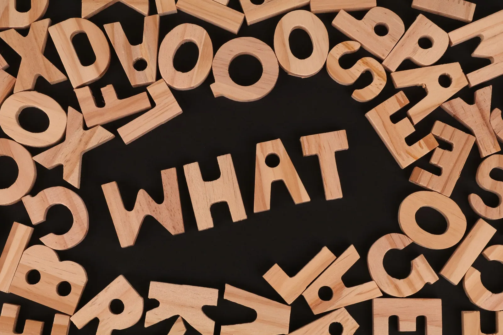 Wooden letters spelling 'WHAT' among scattered letters