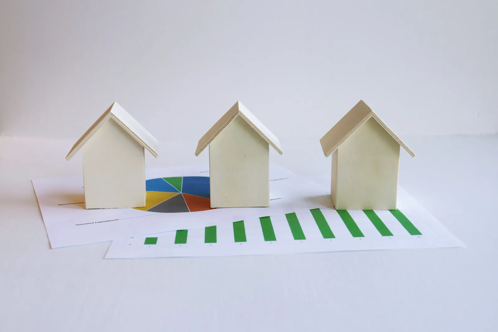 Three white model houses standing on a printed bar chart