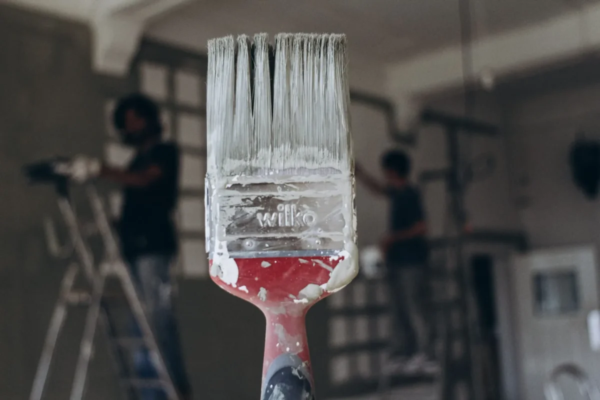 Paintbrush held up in front of painters working in a room