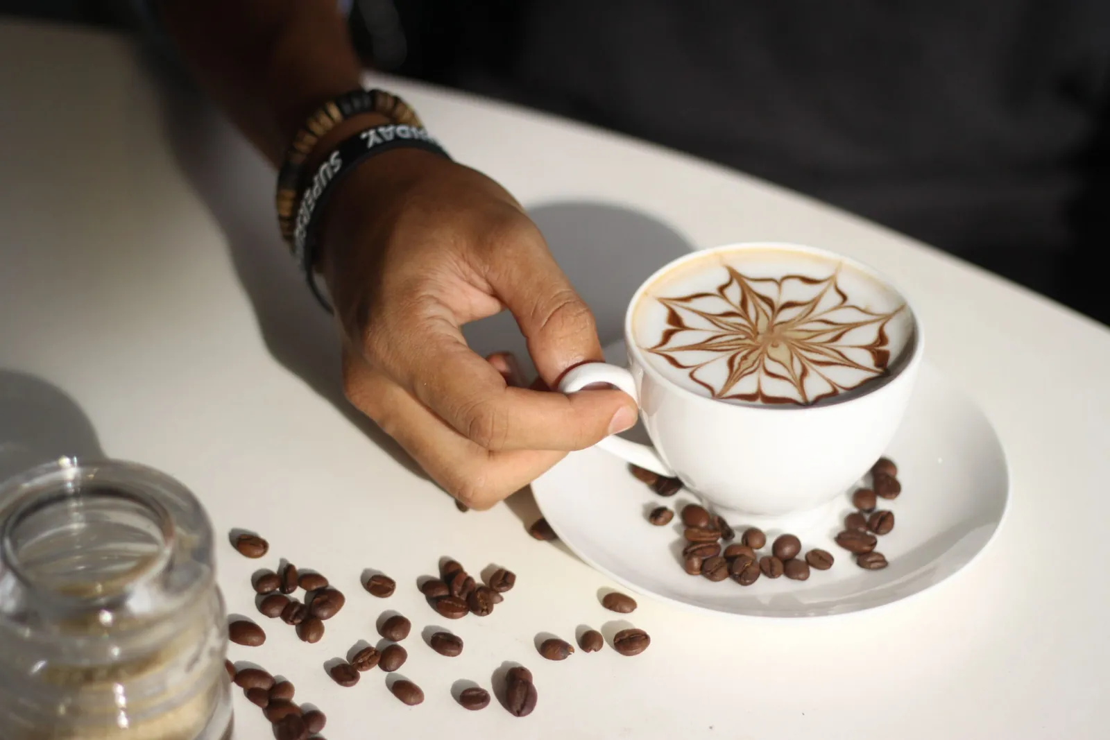Hand holding a cappuccino with latte art beside scattered coffee beans