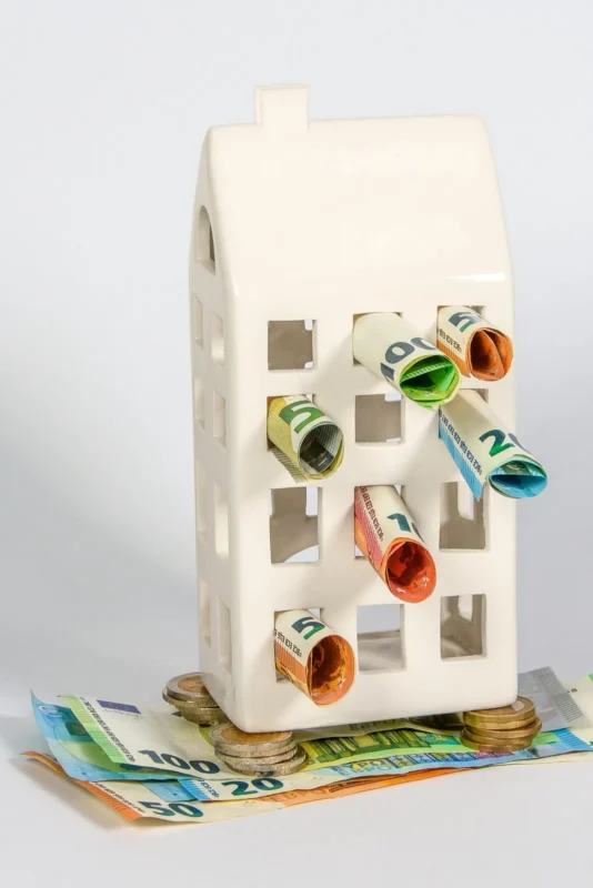 White ceramic house model with rolled banknotes in its windows