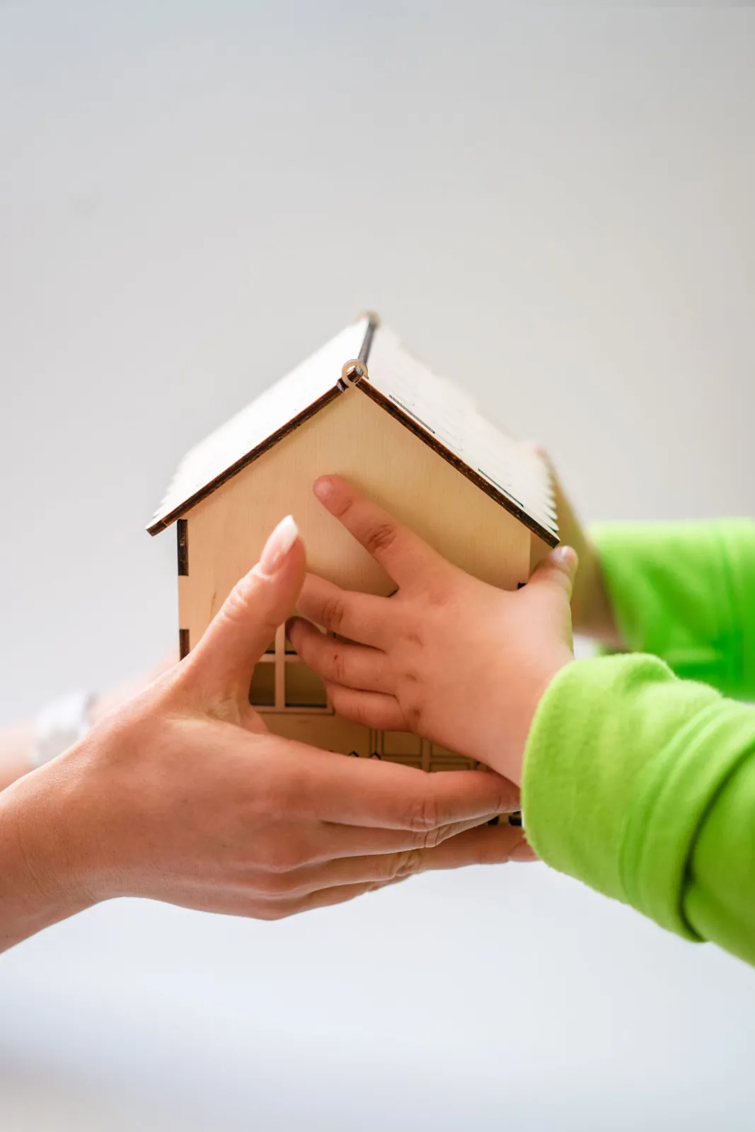 Hands passing a small wooden house to a child