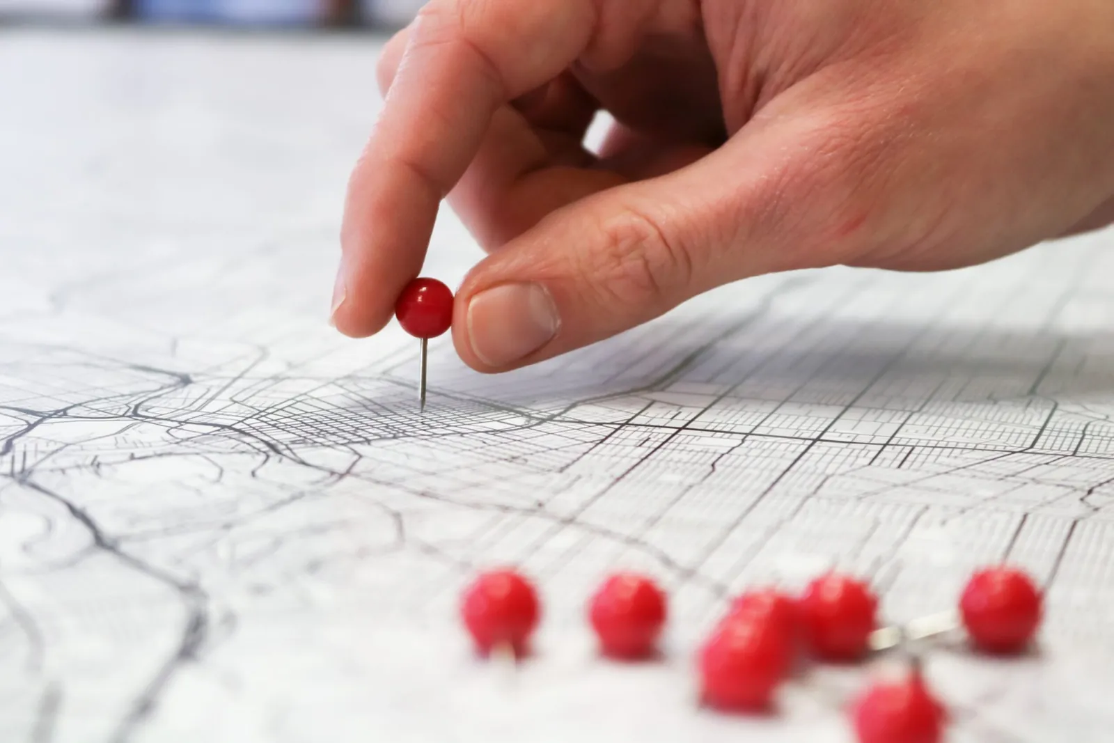 Hand placing red pins on a street map