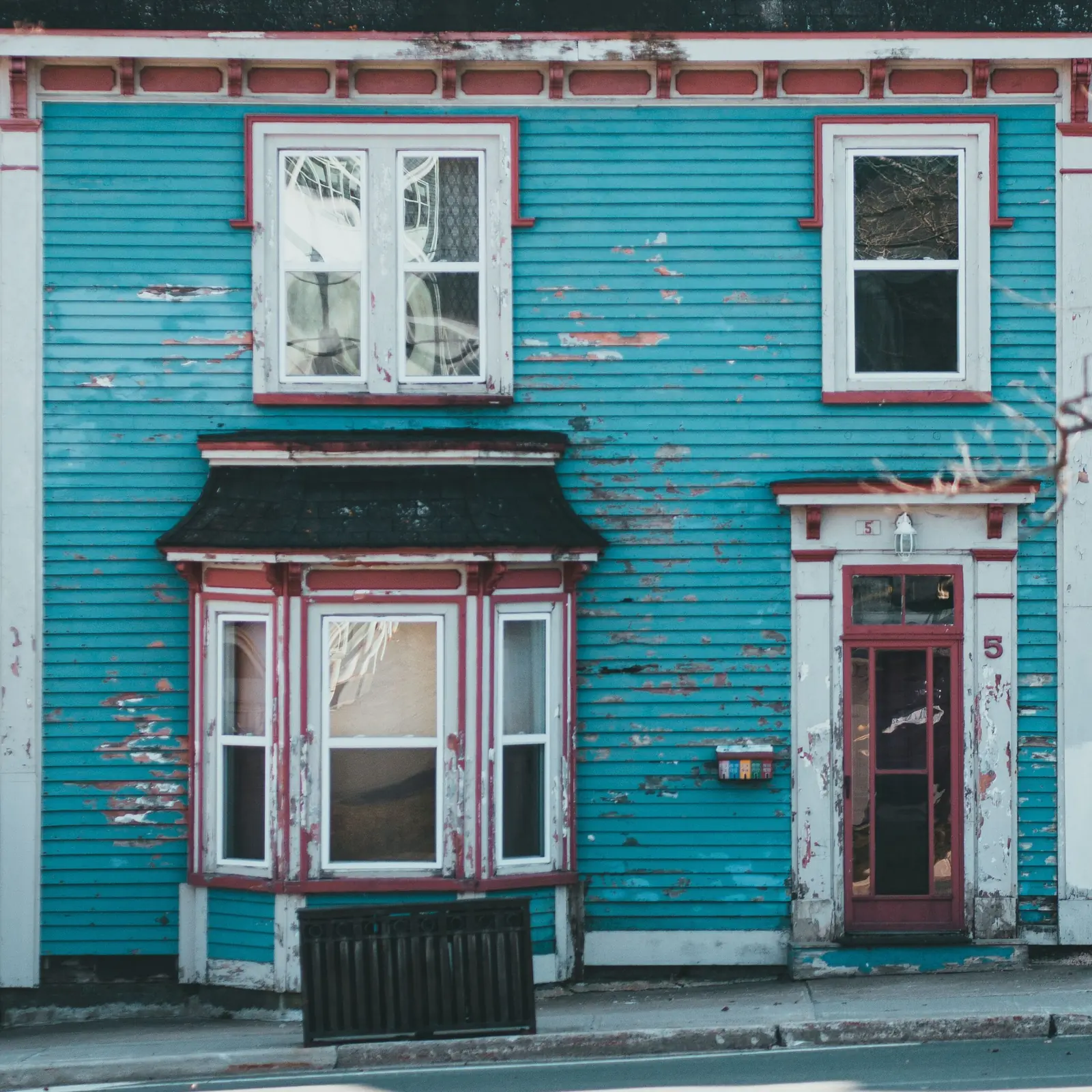 Weathered blue two-story house with a bay window