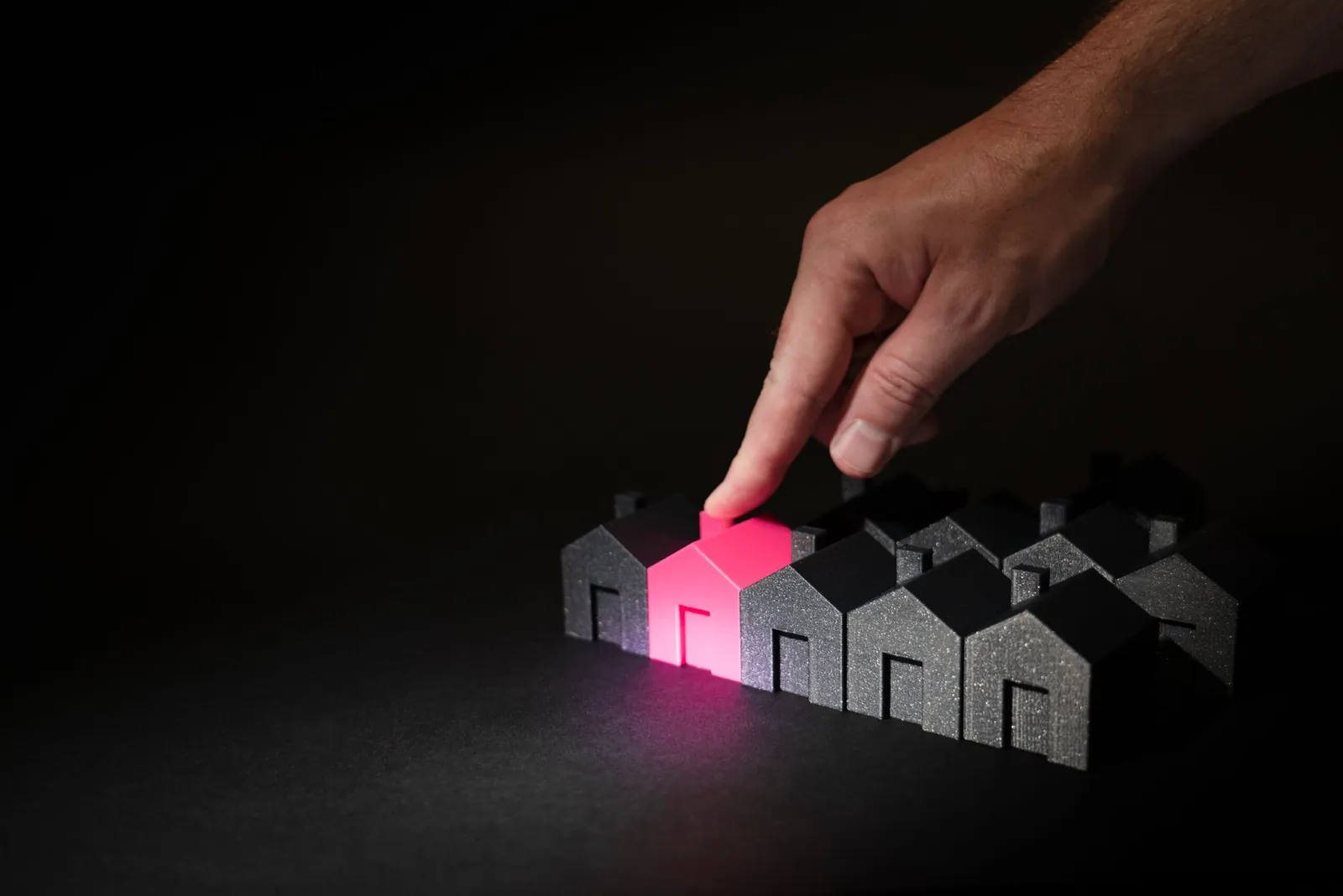 Finger choosing a pink-lit model house from a row of houses
