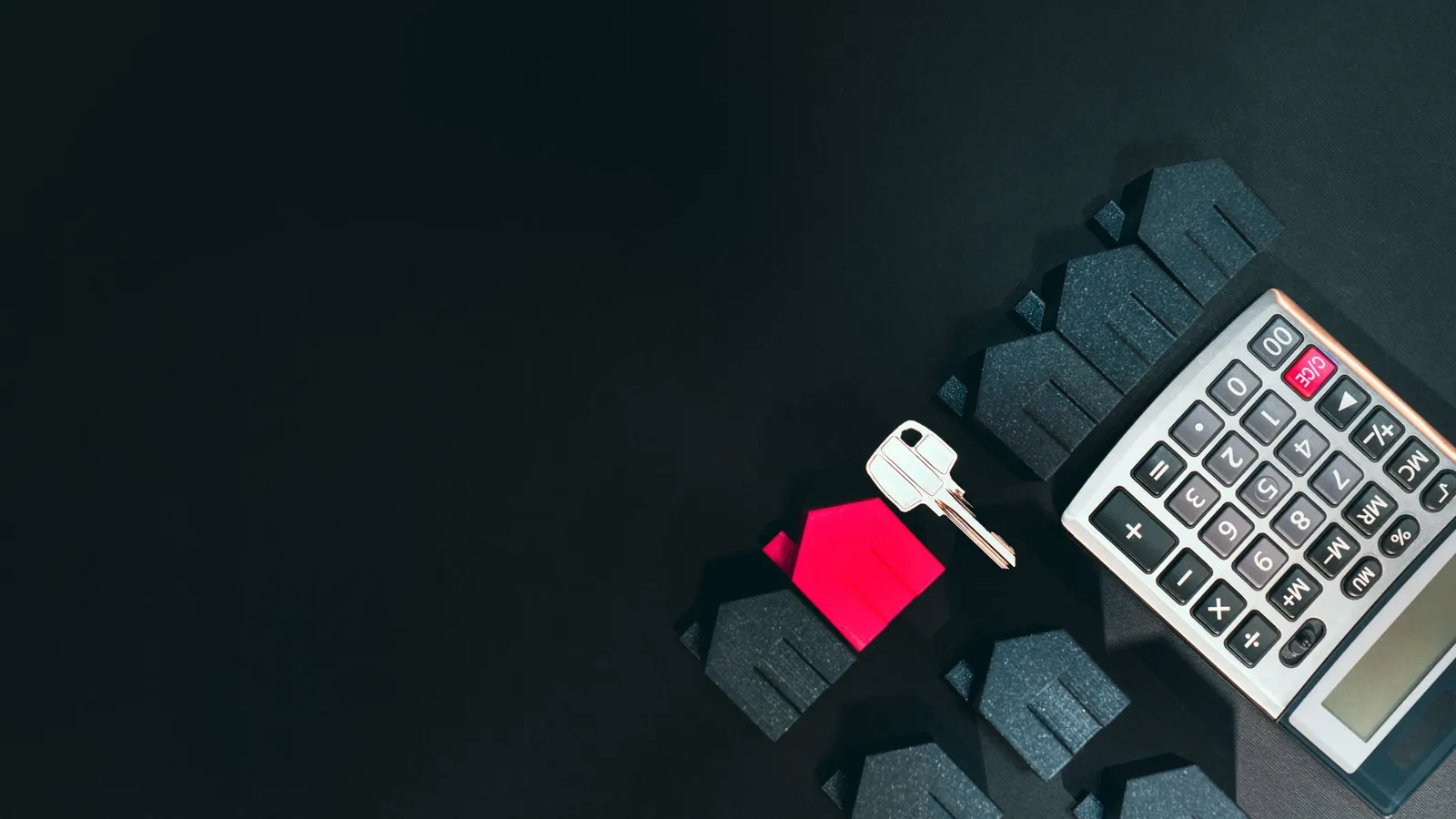 Calculator, keys and a red model house on a dark table