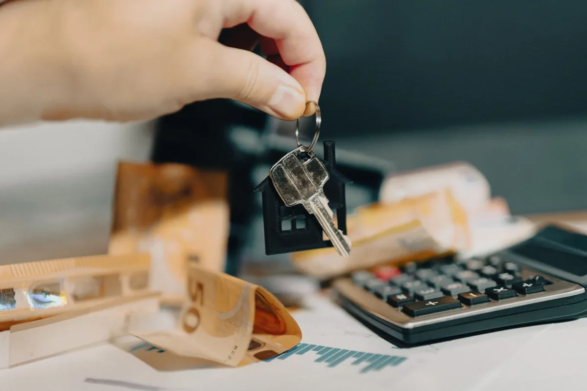 Hand holding keys above a calculator and wooden house blocks
