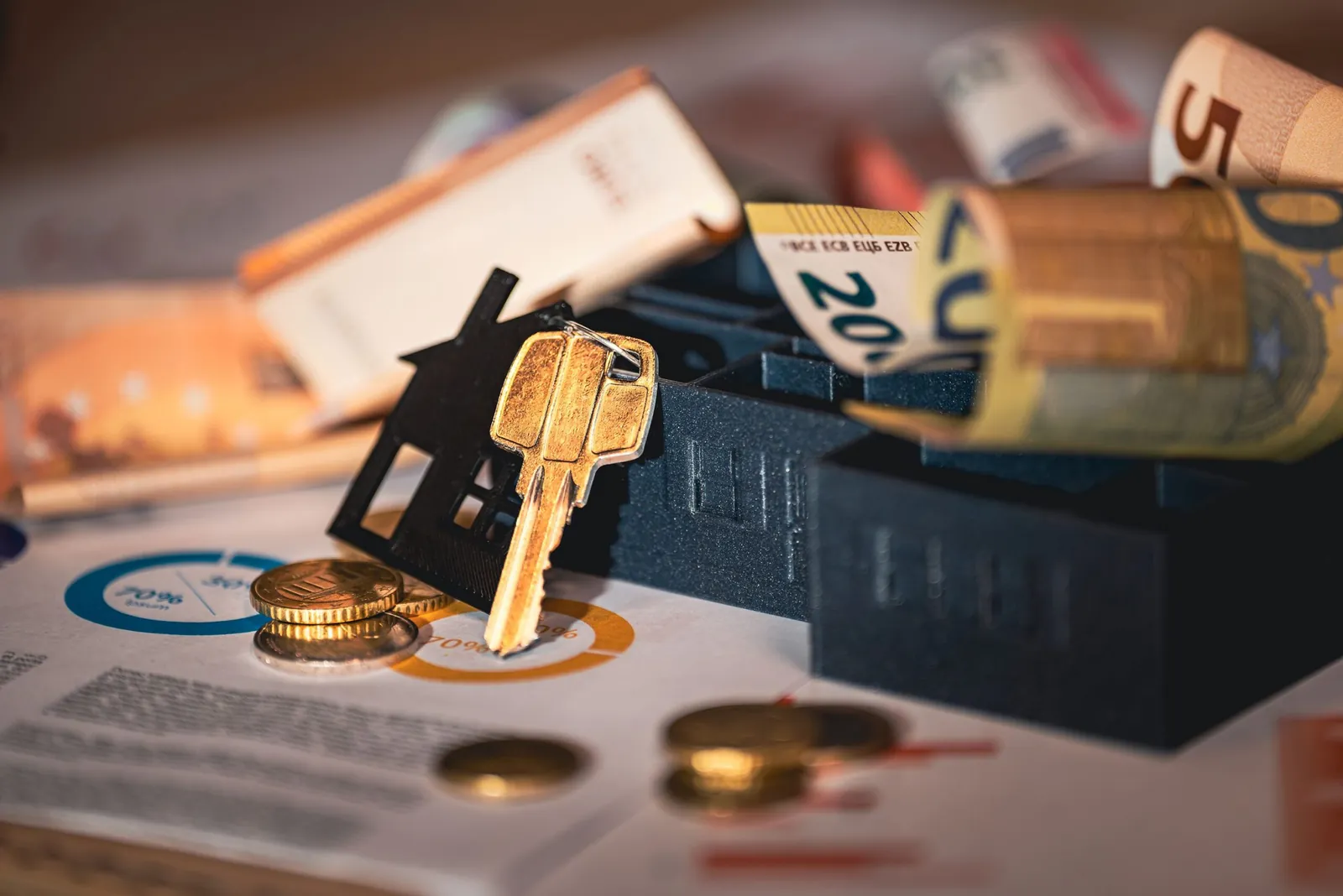 House keys and euro notes beside black model houses on charts
