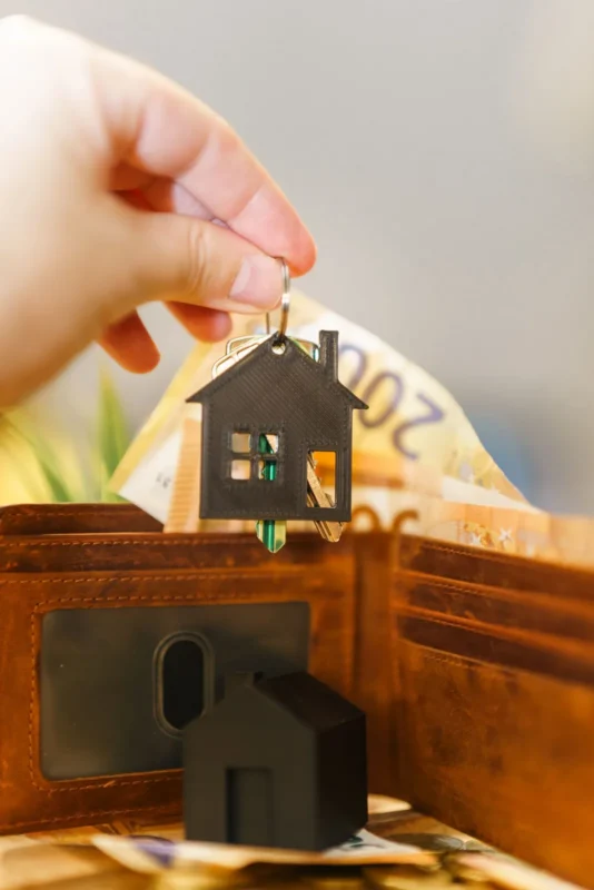 Hand placing a house-shaped keychain into a wallet with cash