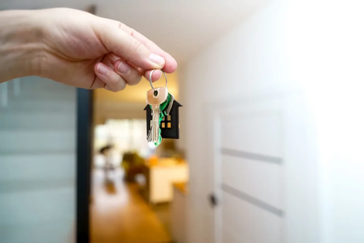 Hand holding house keys inside a bright entryway