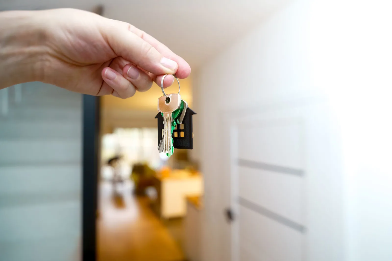 Hand holding house keys inside a bright entryway