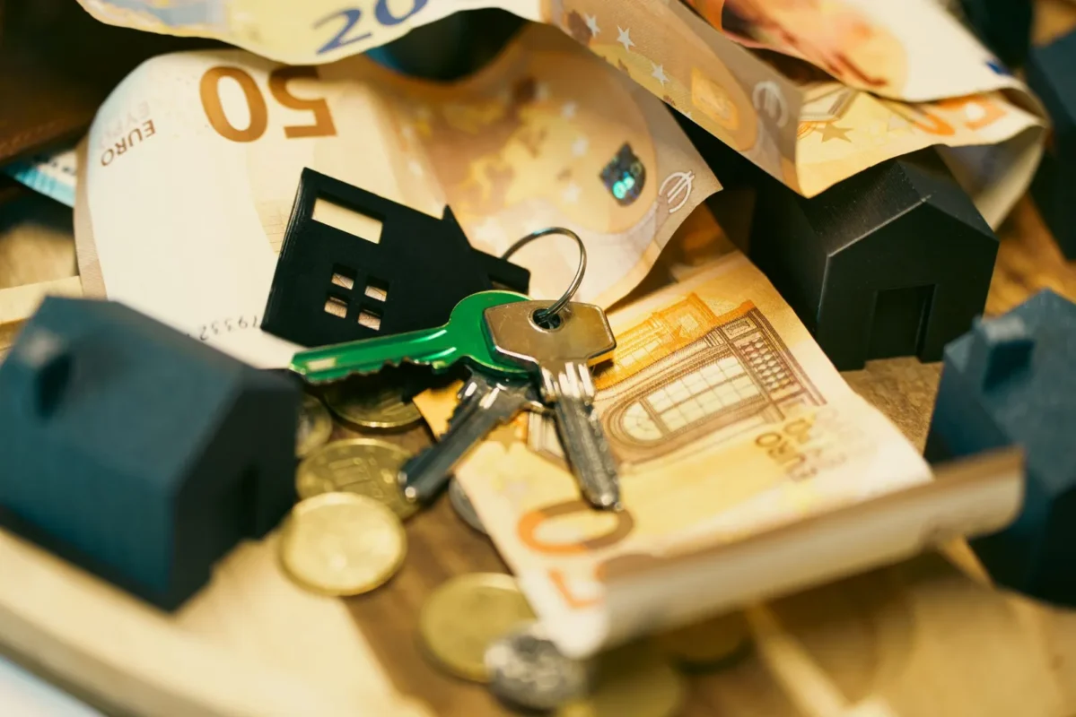 House keys and model houses on a pile of cash and coins