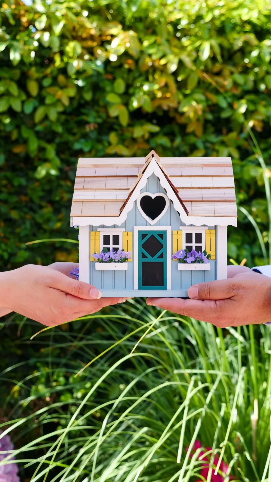 Hands holding a small blue model house over green plants