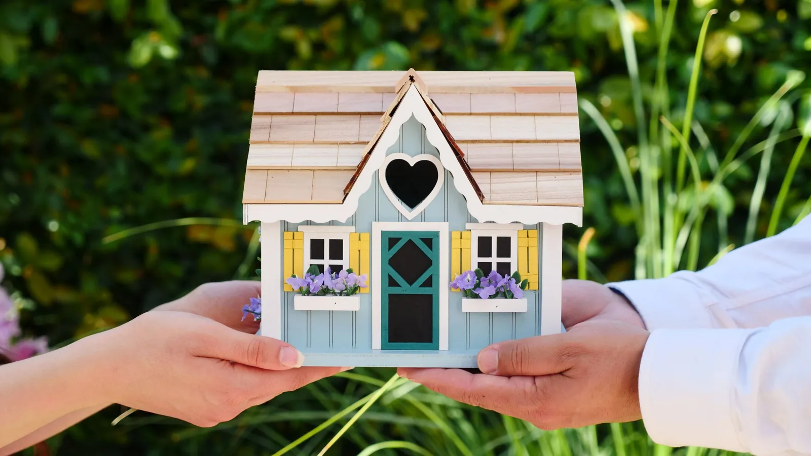 Hands passing a small blue model house