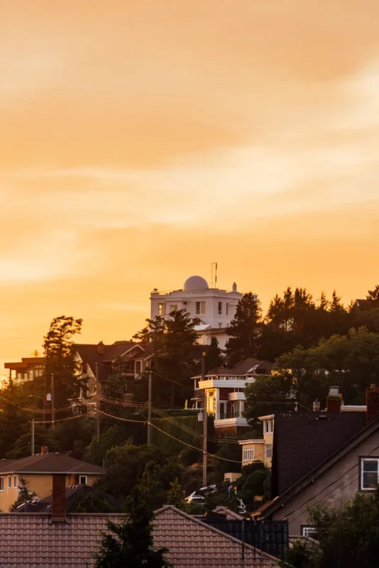 Hillside homes silhouetted against an orange sunset sky
