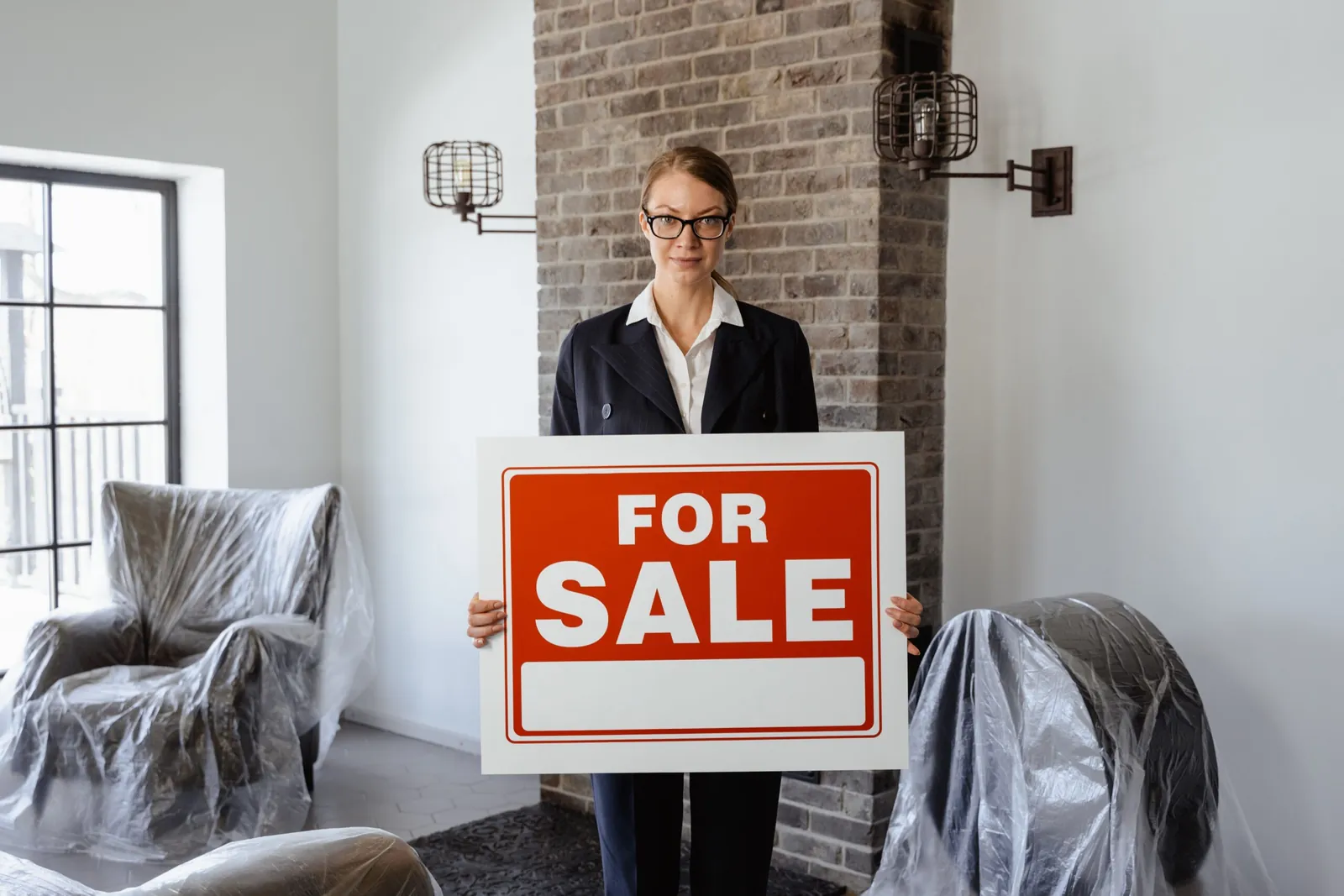 Agent holding a 'For Sale' sign inside a staged home
