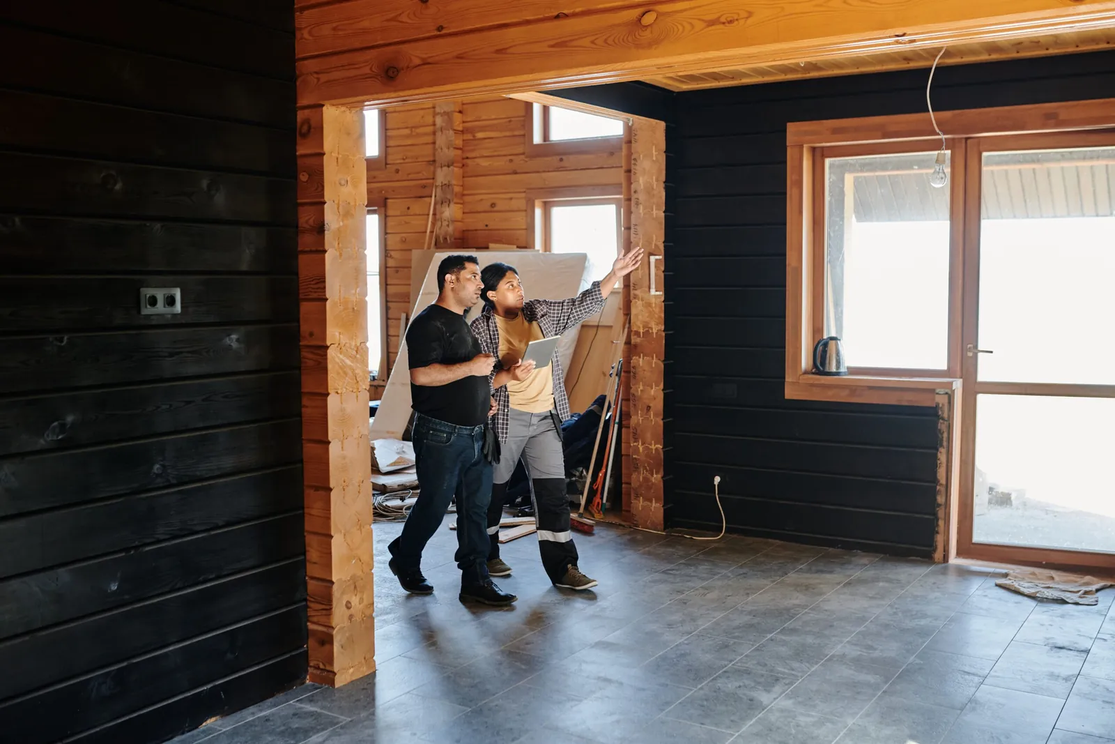 Two people looking over an unfinished room with dark wood walls