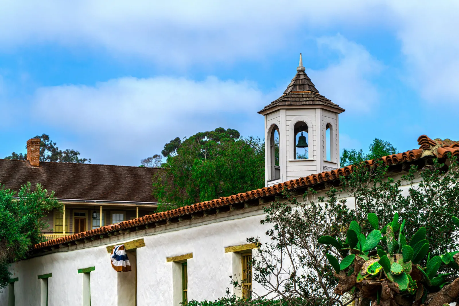 White adobe building with a red clay tile roof and wooden bell tower under a blue sky