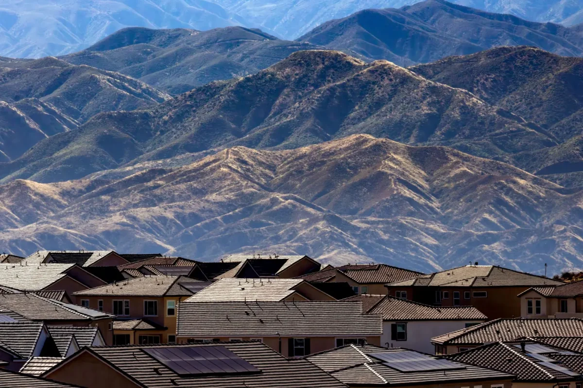 Tile-roofed homes with rooftop solar panels in front of layered dry mountain ridges