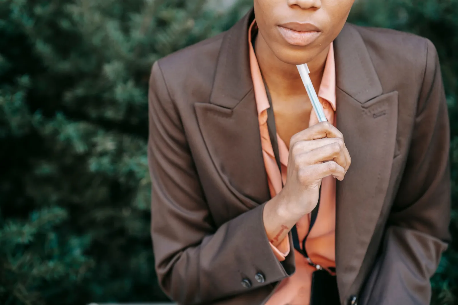Woman in a blazer thinking with a pen to her lips