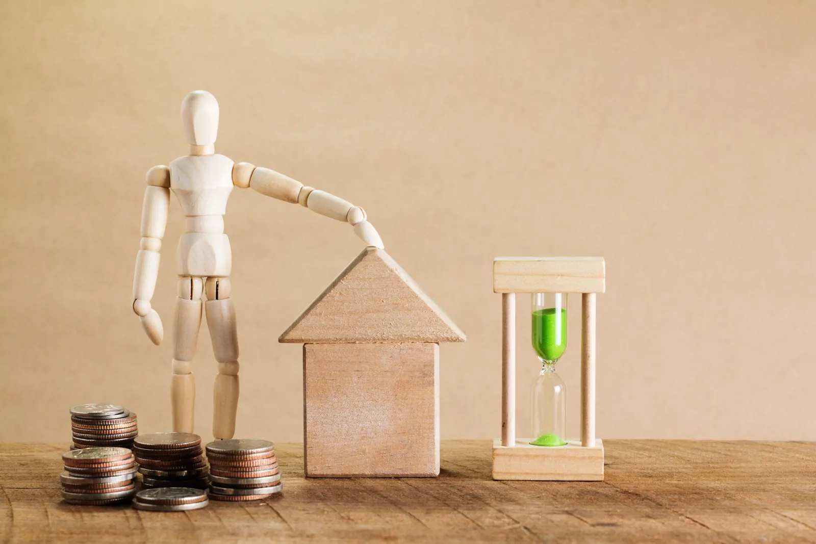Wooden figure resting on a model house beside coins and an hourglass
