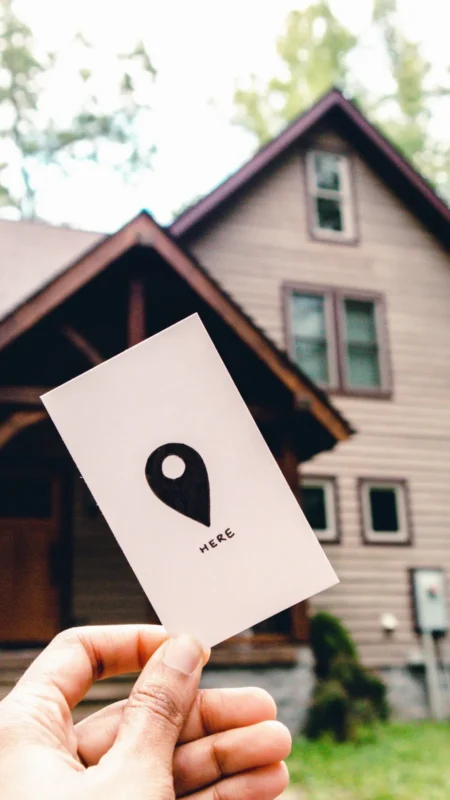 Hand holding a card with a map pin icon in front of a house