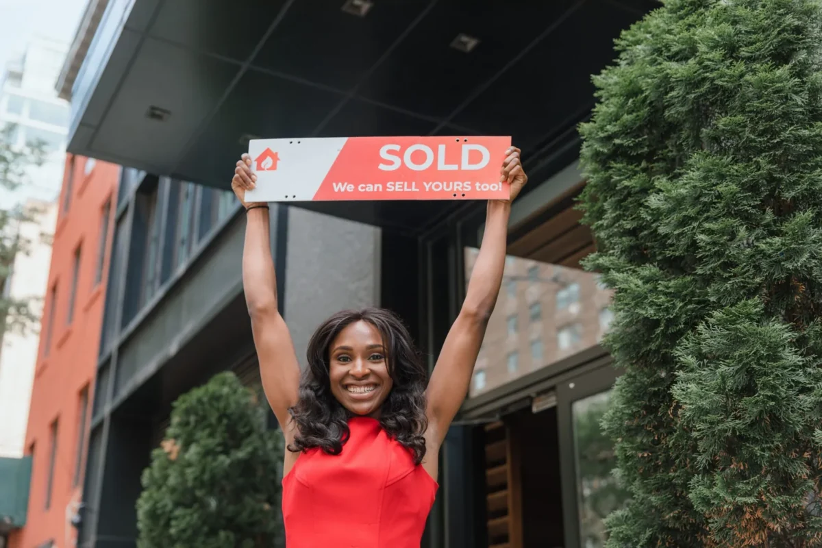 Smiling woman holding a 'Sold' sign overhead