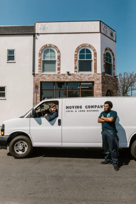 Moving van parked outside a building with two movers