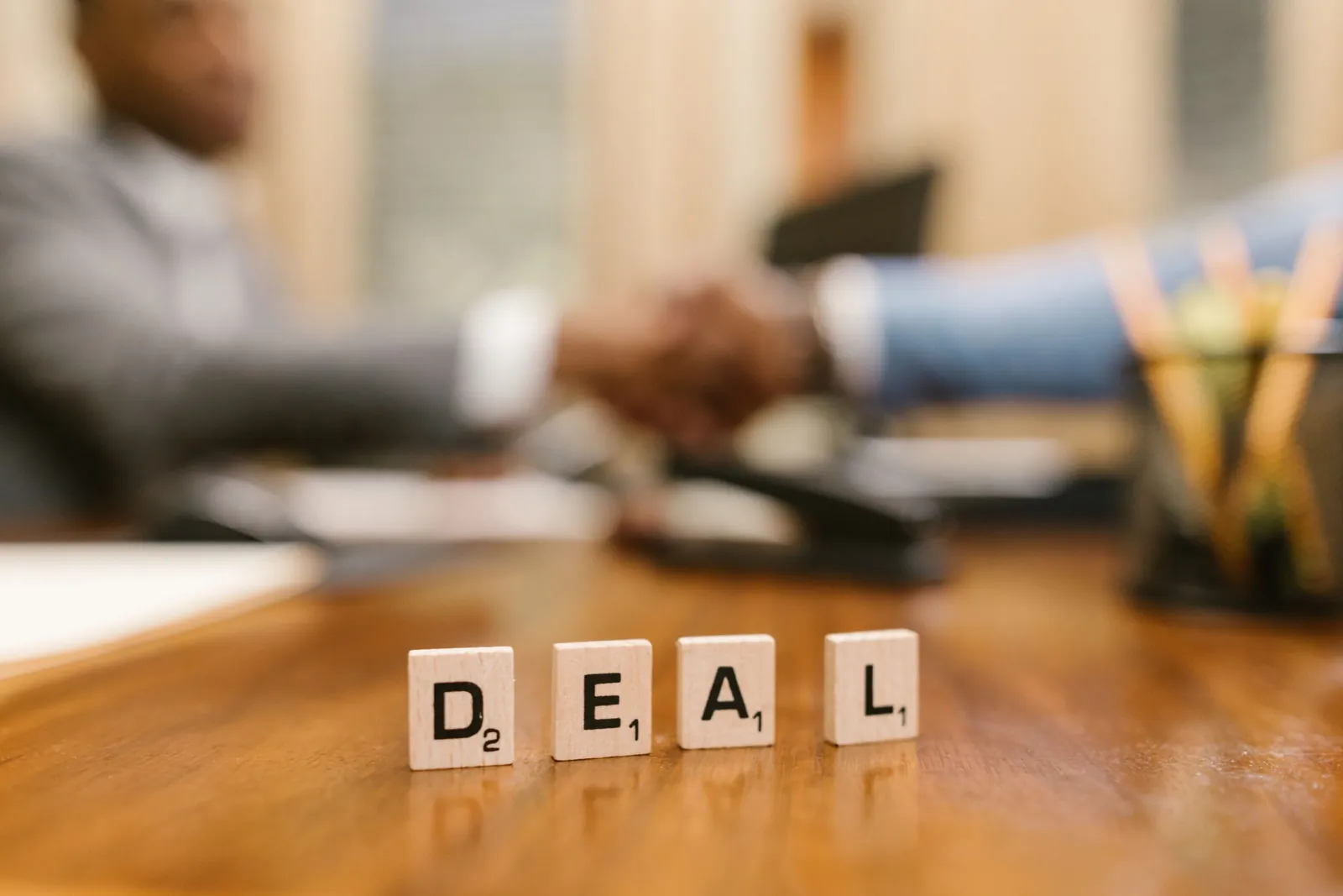 Letter tiles spelling 'DEAL' in front of a handshake