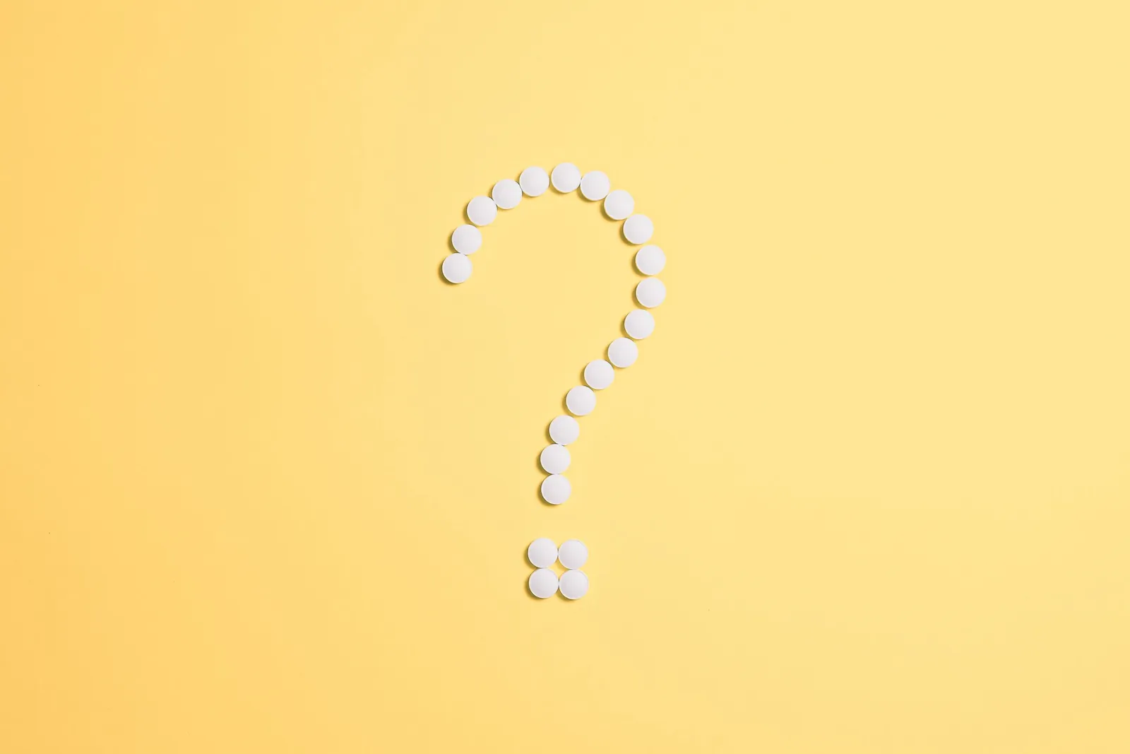 Question mark made of white pills on a yellow background