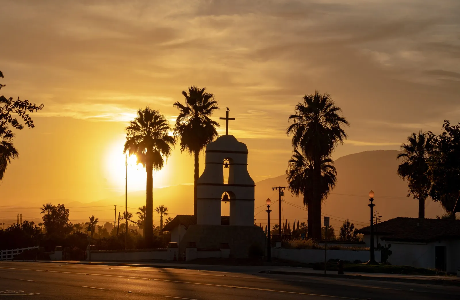 Mission-style bell tower and palm trees silhouetted against a golden sunset