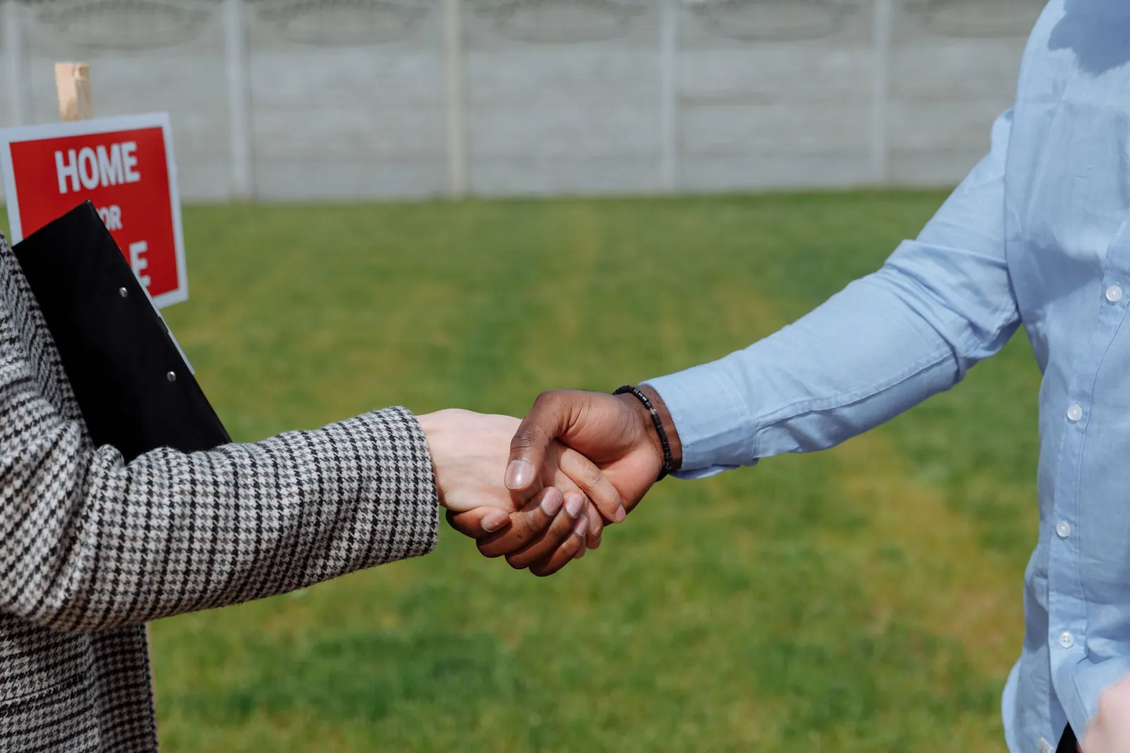 Handshake in front of a 'Home for sale' sign on a lawn