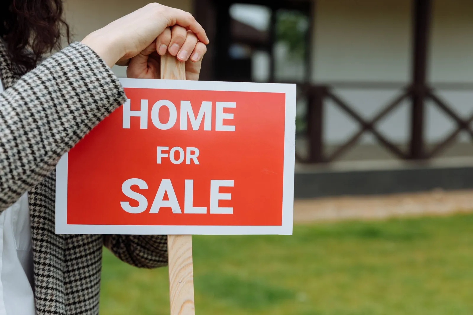Hand holding a 'Home for Sale' sign on a lawn