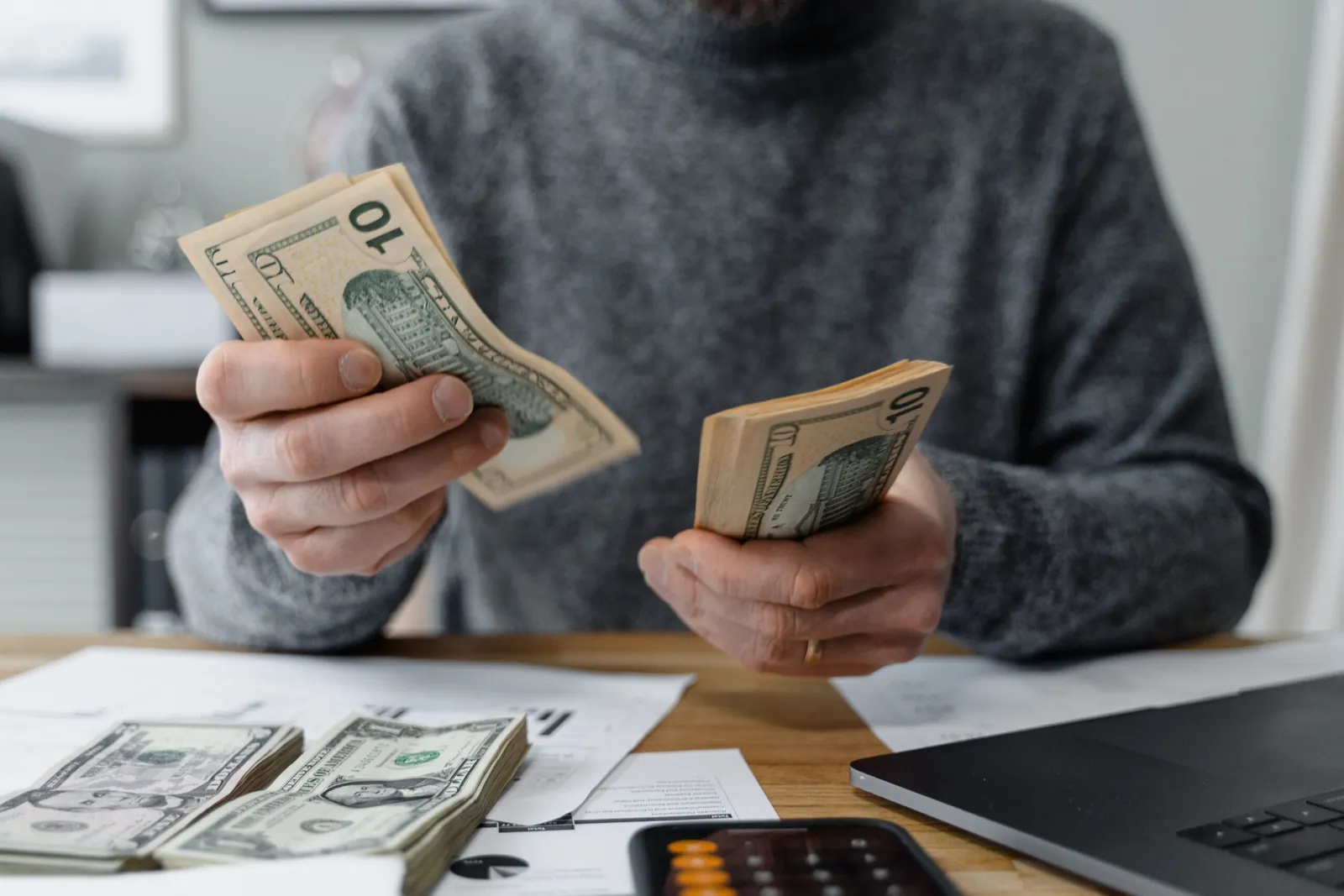 Person counting US dollar bills at a desk