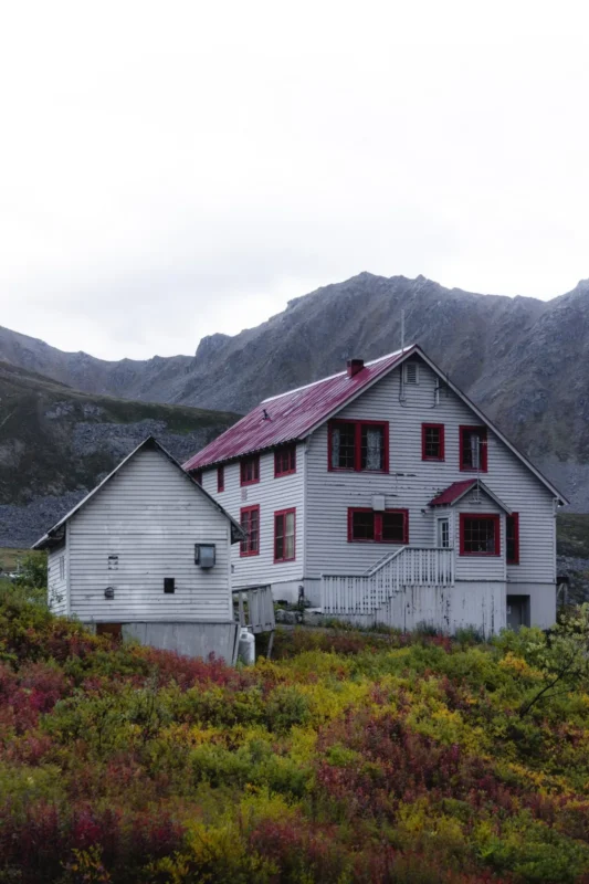 White two-story house with a red roof below misty hills