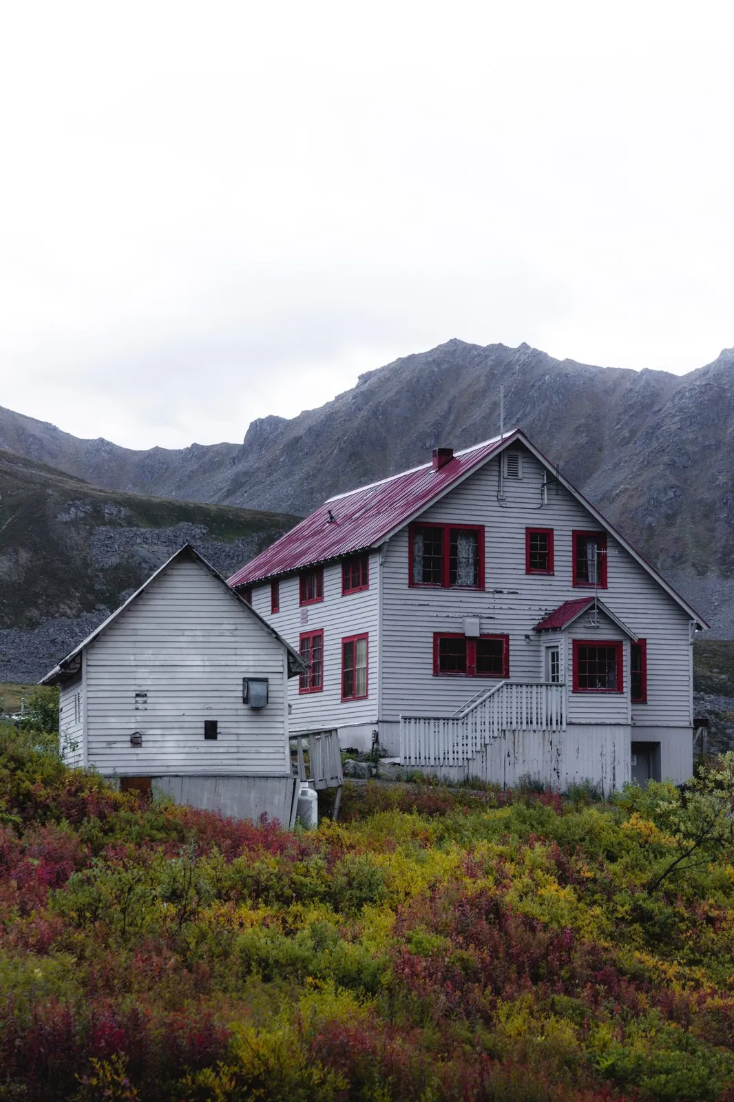 White two-story house with a red roof below misty hills