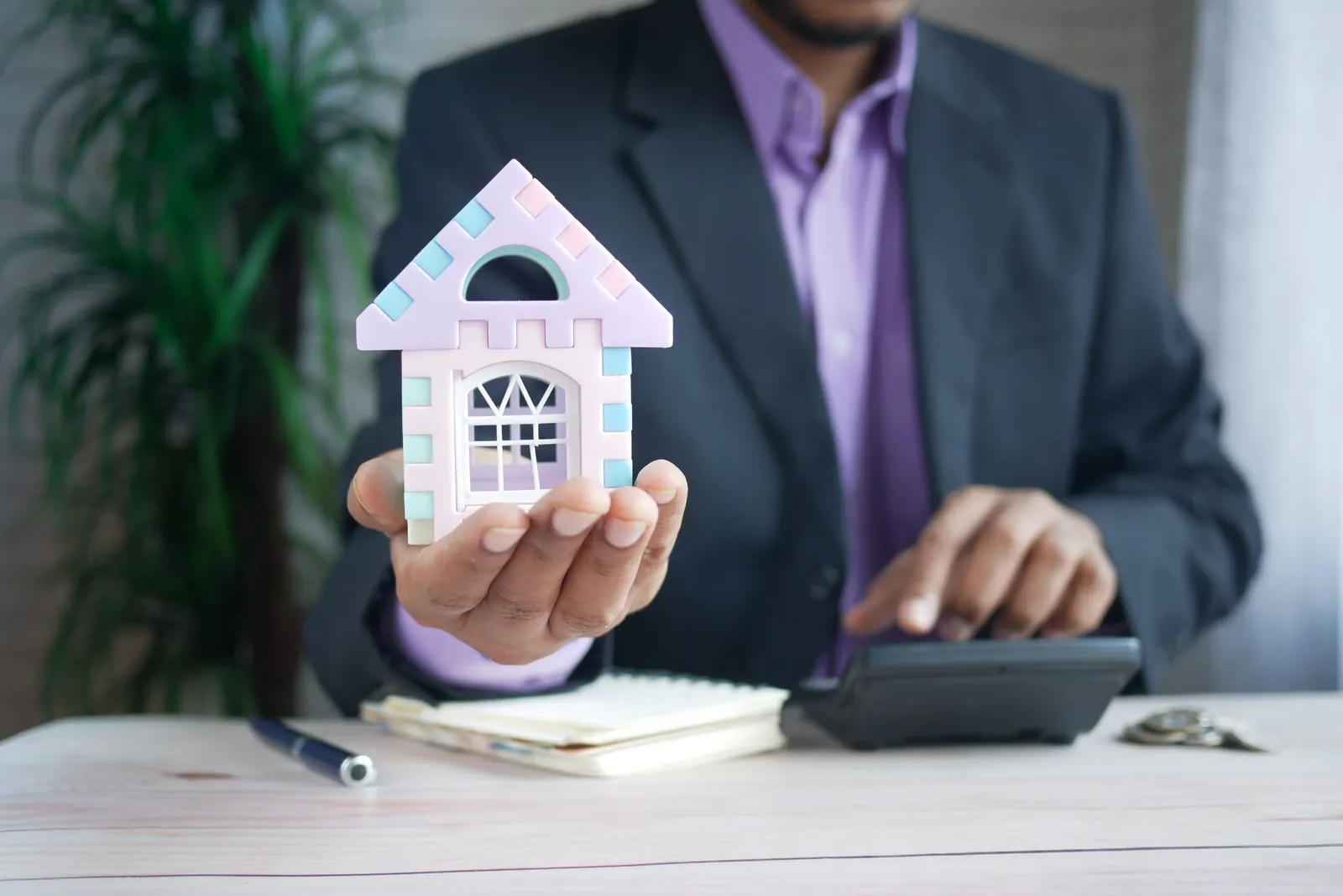 Agent holding a model house while working on a calculator