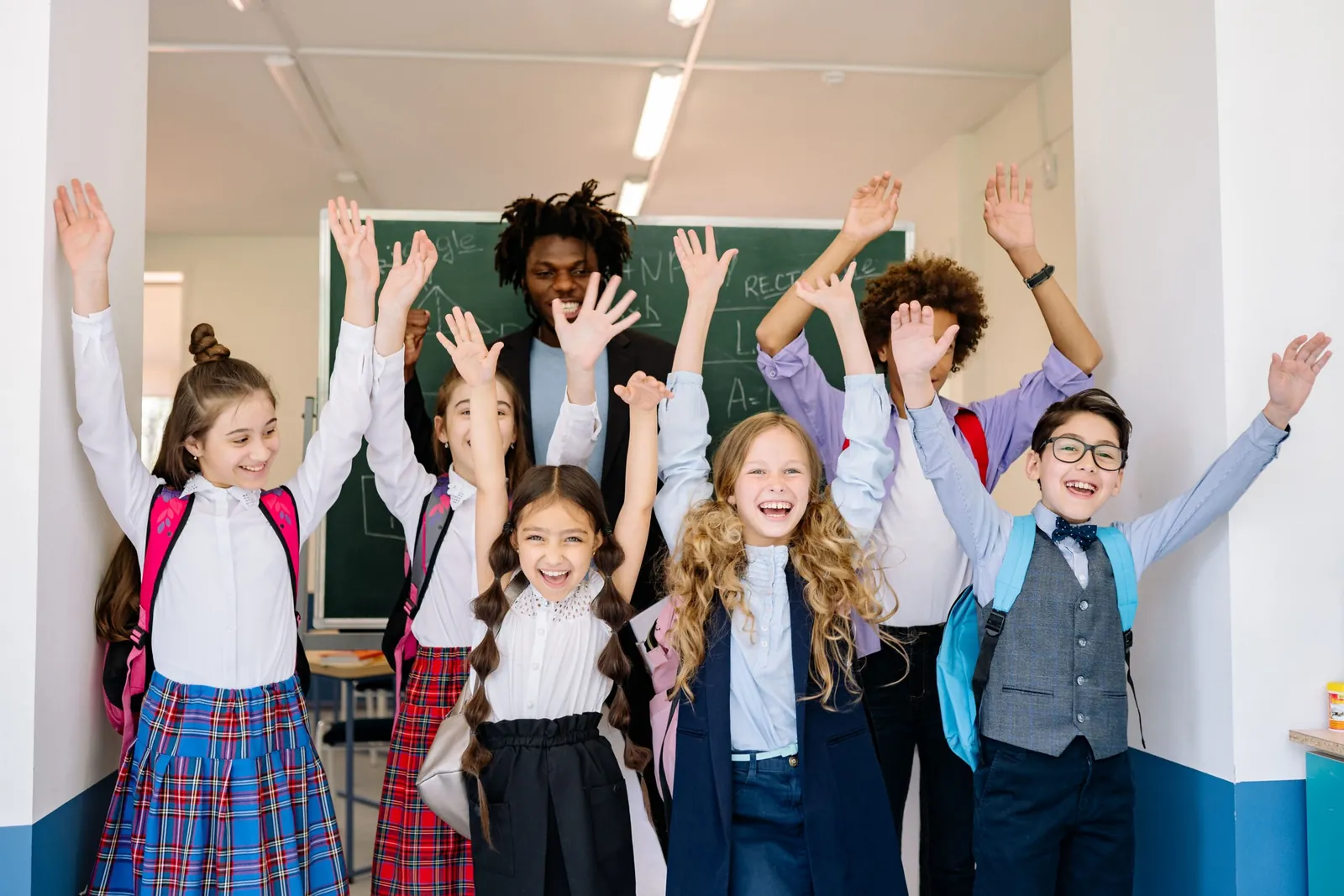 Smiling schoolchildren with backpacks cheering in a classroom