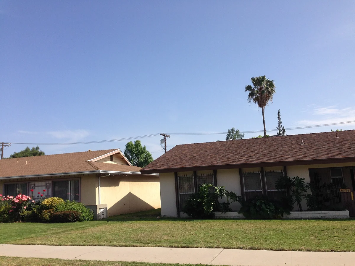Two single-story ranch houses with low-pitched roofs, green lawns and flowering shrubs under a blue sky in Northridge